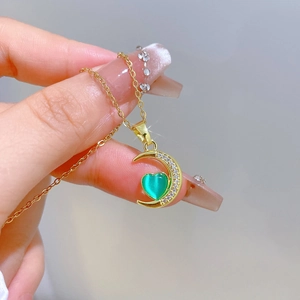 Macro shot of gold moon pendant featuring a green heart stone and sparkling crystals