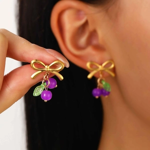 Detail of golden bow earrings with purple beads and green leaves on model