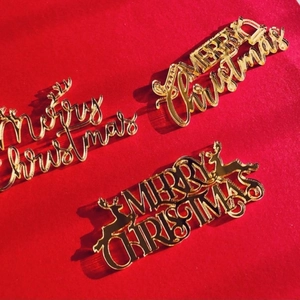Three golden acrylic Merry Christmas cake toppers on a festive red background