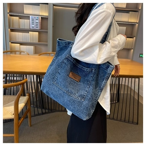 Detail of vintage blue denim tote bag with brown leather logo patch and large pocket
