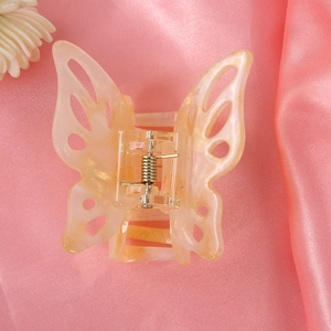 Detail view of a translucent champagne yellow butterfly hair claw clip on pink silk