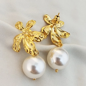 Minimalist gold leaf earrings with white round pearls on white knit fabric background