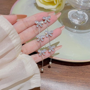 Macro view of silver bow-knot tassel earrings with rhinestones held in hand