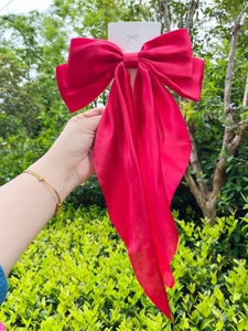 Detail of a large red satin bow hair clip with elegant long ribbons in natural lighting