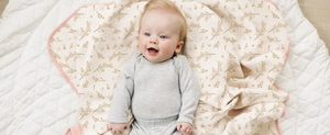 Soft pink floral cotton baby swaddle blanket with hemmed edges on a quilted mat