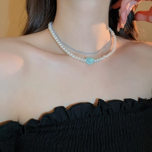 Detail of double-layer necklace with white pearls, blue beads and a heart pendant
