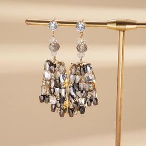 Detailed view of bohemian gold tassel earrings with gray crystals on a display stand