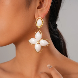 Close-up of elegant gold four-leaf clover drop earrings with white petals on a model
