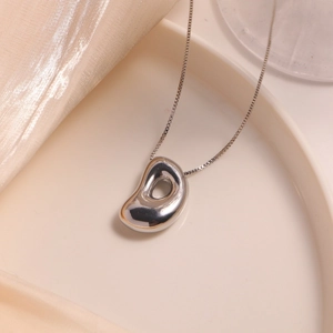 Polished silver bean pendant necklace on a delicate chain displayed on white tray