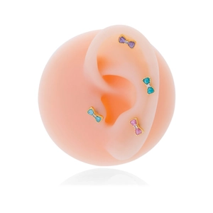 Golden bow-shaped stud earrings set with colorful glitter stones on a silicone model