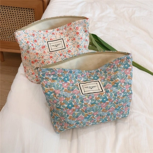 Floral canvas makeup bag with zipper closure and white woven label on white bedding