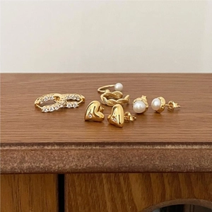 Close-up of gold heart earrings, pearl studs, and zircon ring on a rustic wooden surface