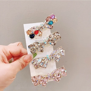 Close-up of four gold hair clips with colorful rhinestones on a white card display