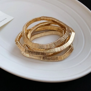 Close-up of layered gold snake chain bracelets with textured finish on a ceramic tray