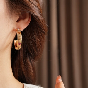 Close-up of model wearing C-shaped gold earrings with colorful rhinestones in a side view