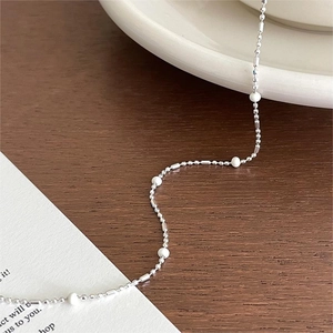 Minimalist 925 sterling silver necklace with irregular white beads on a wooden desk