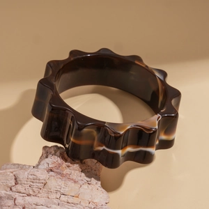 Detail of wide wave-edged acrylic bangle in amber swirl resting on a natural stone