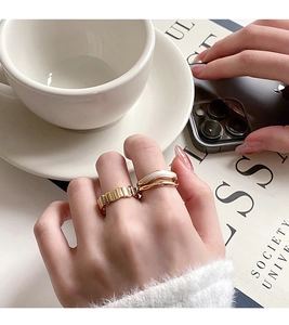 Close-up of gold layered rings with white enamel and gear texture worn by a model
