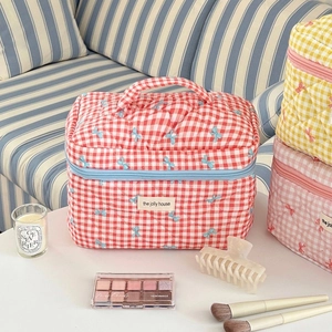 Detailed close-up of quilted red checkered makeup bag with blue bow embroidery and top handle