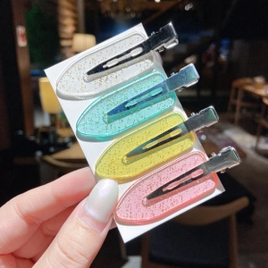 Close-up of four colorful glitter hair clips in white, green, yellow, and pink on a card