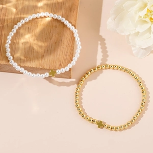 Cross charm pearl and gold bead layered bracelet set displayed on a wooden base