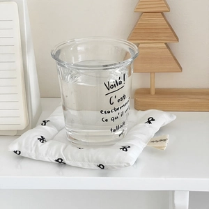 Close-up of a bow-patterned padded fabric coaster with a clear glass on a minimal desk