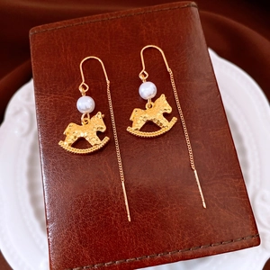 Detailed close-up of a golden rocking horse earring with a white pearl on a leather stand