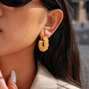 Gros plan d'un modèle portant une boucle d'oreille créole en maille plissée dorée 24k