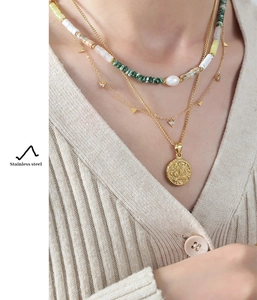 Detail of layered gold necklaces with triangle pendant, beads, and pearl on model