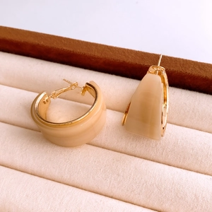 Gros plan de boucles d'oreilles créoles en résine beige avec bordure dorée en boîte