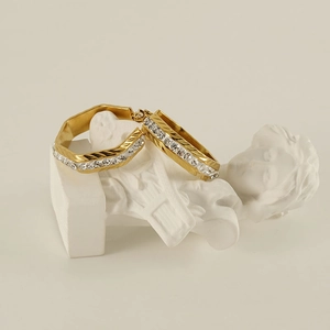 Detailed view of gold geometric hoop earrings with crystals on a white pedestal