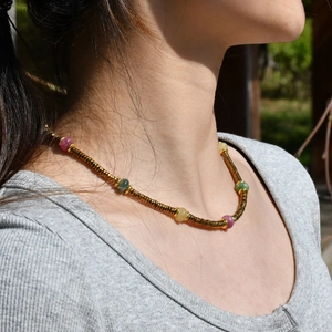 Close-up of a gold spiral chain necklace with colorful tourmaline beads on a woman neck