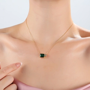 Gold necklace featuring emerald rectangle and clear round gems on female model