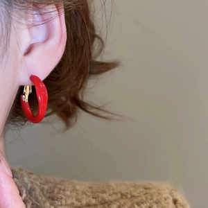 Close-up of red enamel geometric hoop earrings worn by a model in a warm setting