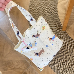 Detail of dachshund print tote bag in cream canvas with plush dog pendant accessory
