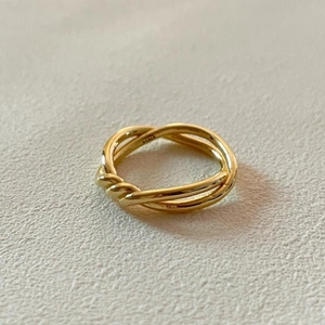Macro d'une bague nœud entrelacée en argent 925 doré sur une surface en pierre texturée