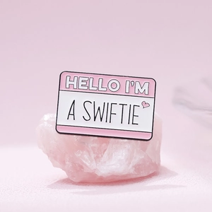 Detailed view of pink enamel 'A SWIFTIE' brooch pin resting on a decorative quartz stone