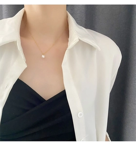 Detail view of a genuine white pearl pendant on a delicate gold chain worn by a model