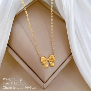 Detail of gold bow necklace pendant with dimensions 1.4x1.1cm on beige display mat