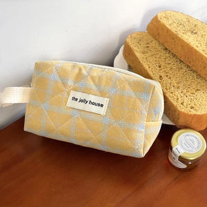 Quilted yellow checkered cosmetic bag with handle and zipper in a cozy home setting
