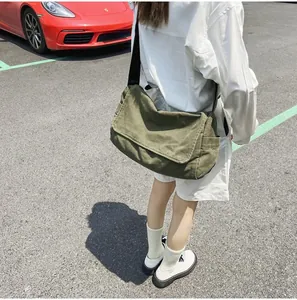 Outdoor street style view of a large army green canvas messenger bag with wide strap