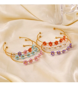 Detail of gold metal bracelets with colorful crystal flowers on beige silk fabric