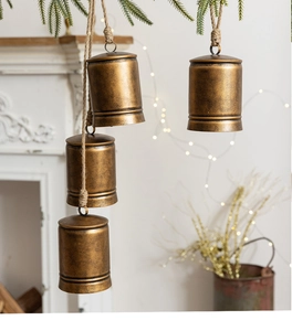 Detail of four vintage bronze metal bells hanging on jute rope against a festive fireplace