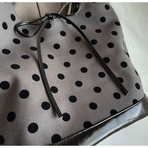 Detailed close-up of grey polka dot canvas fabric with black patent leather bow detail