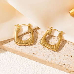 Close-up of golden irregular textured earrings with unique fold pattern on a cream fabric