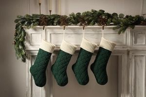 Close-up of four green knitted Christmas stockings with beige cuffs hanging on a festive fireplace