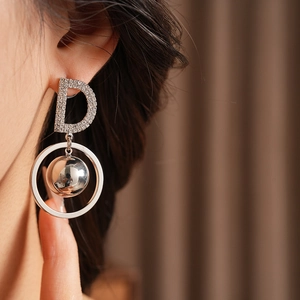 Close-up of silver-tone round hoop earrings with crystal-paved letter D and metal ball