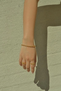 Detail shot of golden twisted chain bracelet and minimalist rings on model's wrist