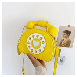 Close-up of creative yellow patent leather retro phone-shaped crossbody bag with dial