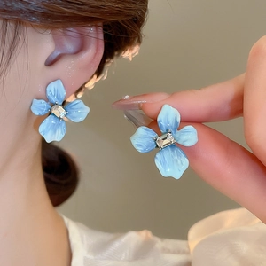 Détail macro d'une boucle d'oreille fleur bleue avec zircon central et pétales en émail doux